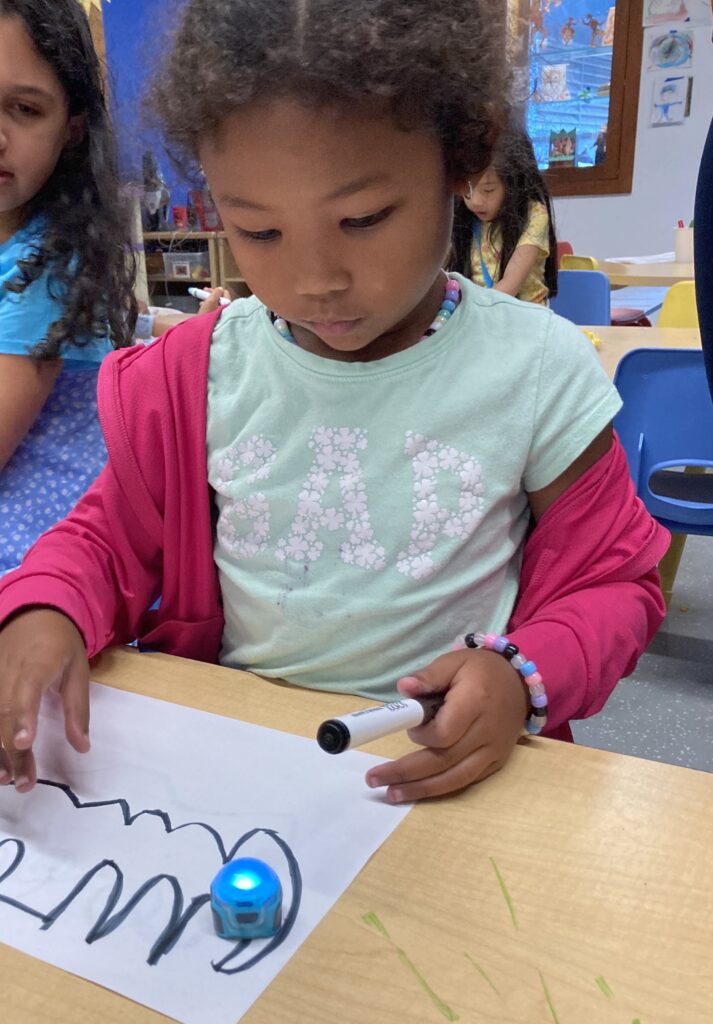 A child holding a marker with a squiggly line on the paper
